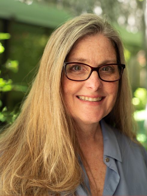 A woman wearing glasses and a white shirt is smiling for the camera.
