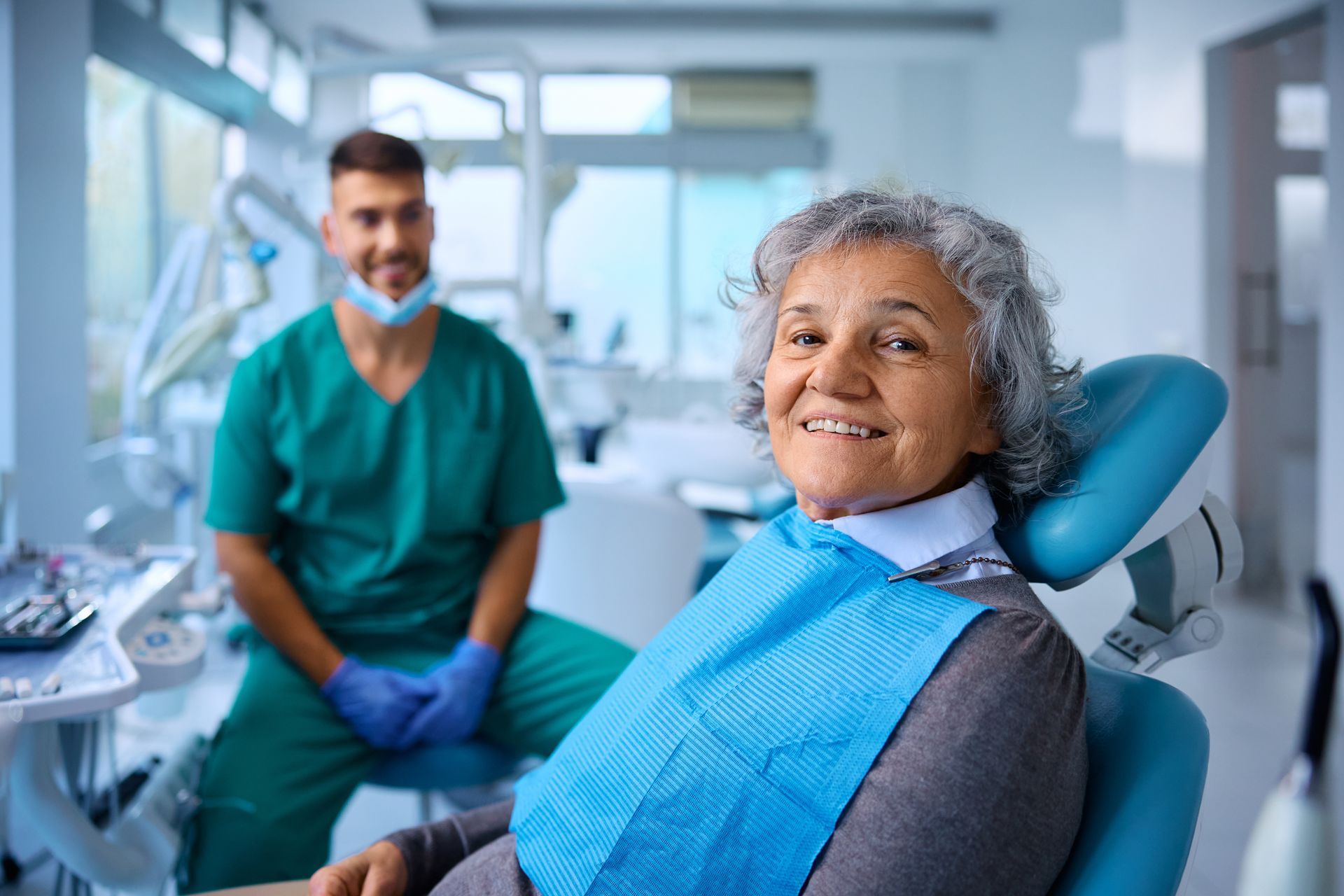 An elderly woman is looking at her teeth in a mirror at the dentist.
