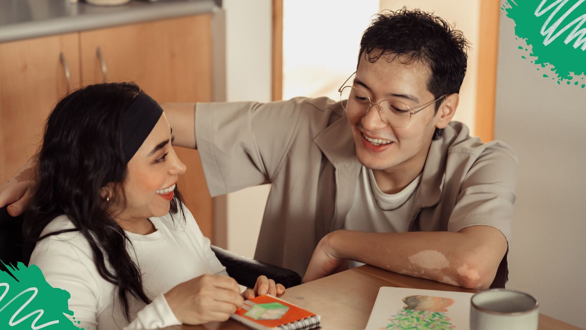 A smiling support worker sits beside a participant engaging in creative arts, demonstrating person-centred NDIS care and capacity building.