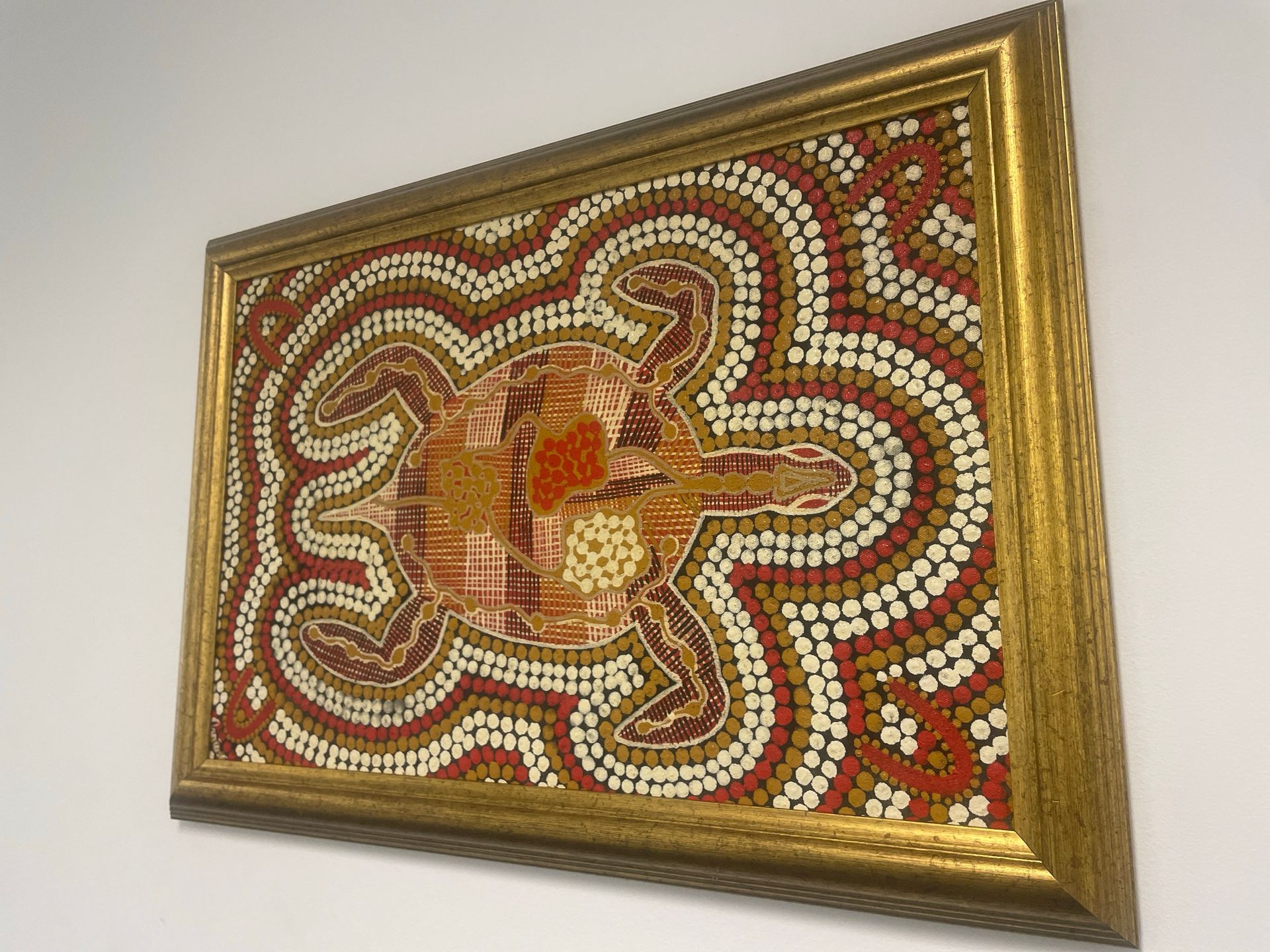 A mosaic painting is hanging on a wall in a gold frame.