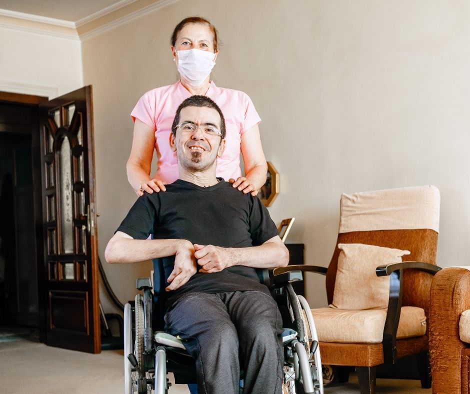 A smiling NDIS participant and a support nurse in a domestic setting, representing the coordination of high-level in-home nursing and complex care to bridge the gap from a hospital discharge team to a reliable daily routine in a safe, stable home.