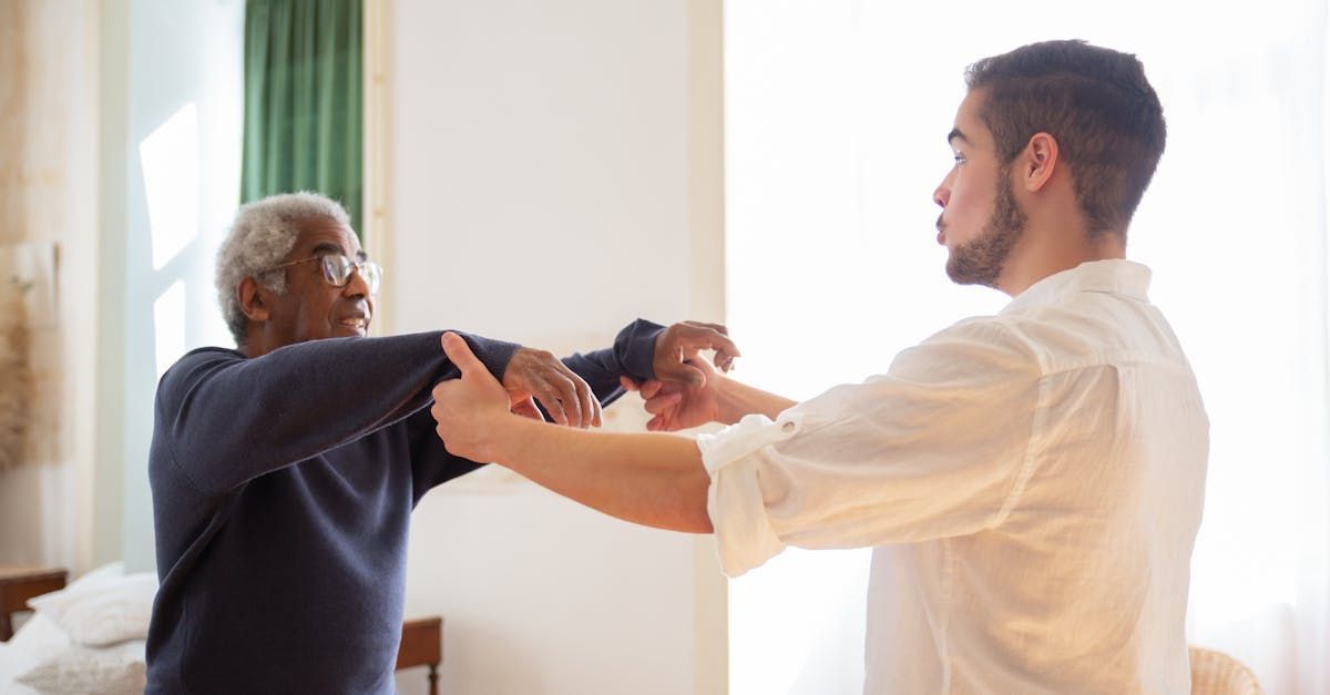 A young man is helping an older man stretch his arms.