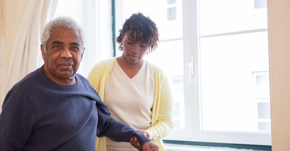 A woman is helping an elderly man walk in a room.