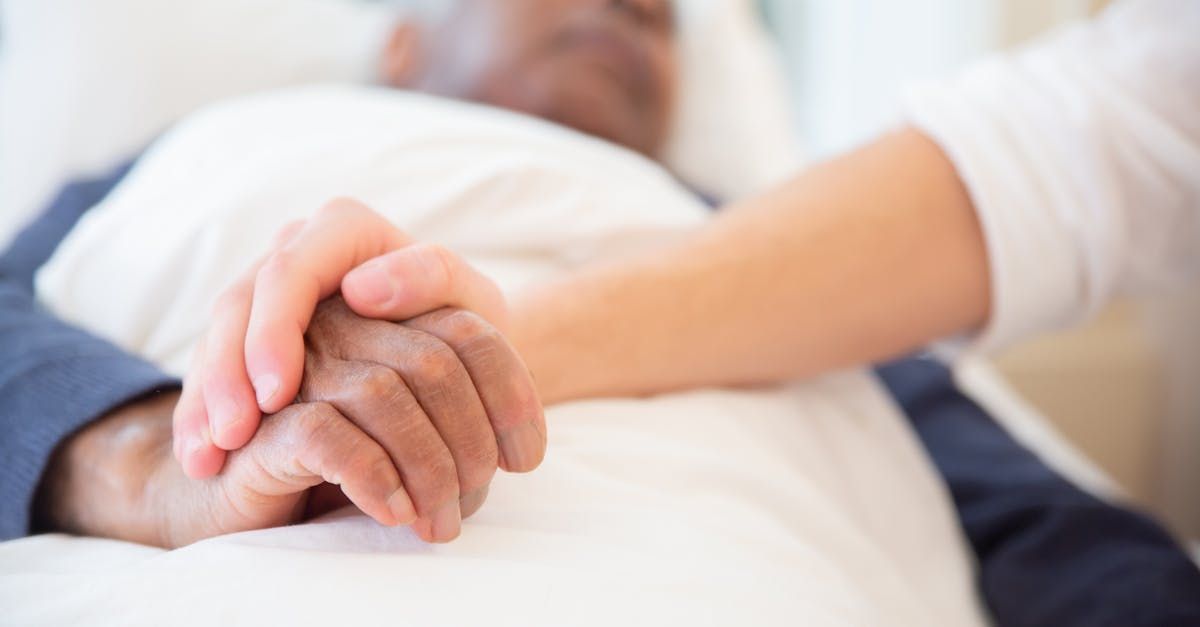 A woman is holding the hand of an elderly man in a hospital bed.