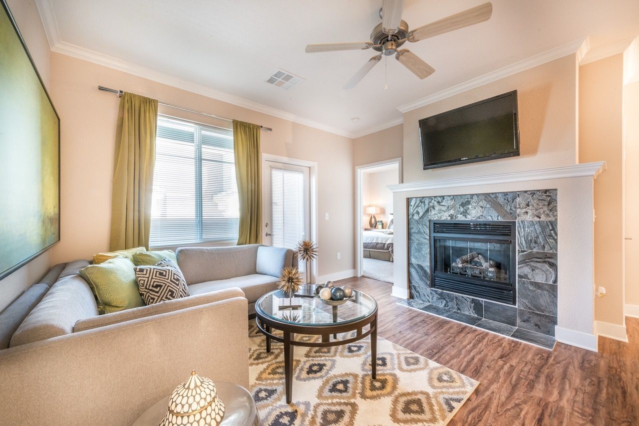 Living room with beige sectional, glass coffee table, fireplace, mounted TV, and wood floors.