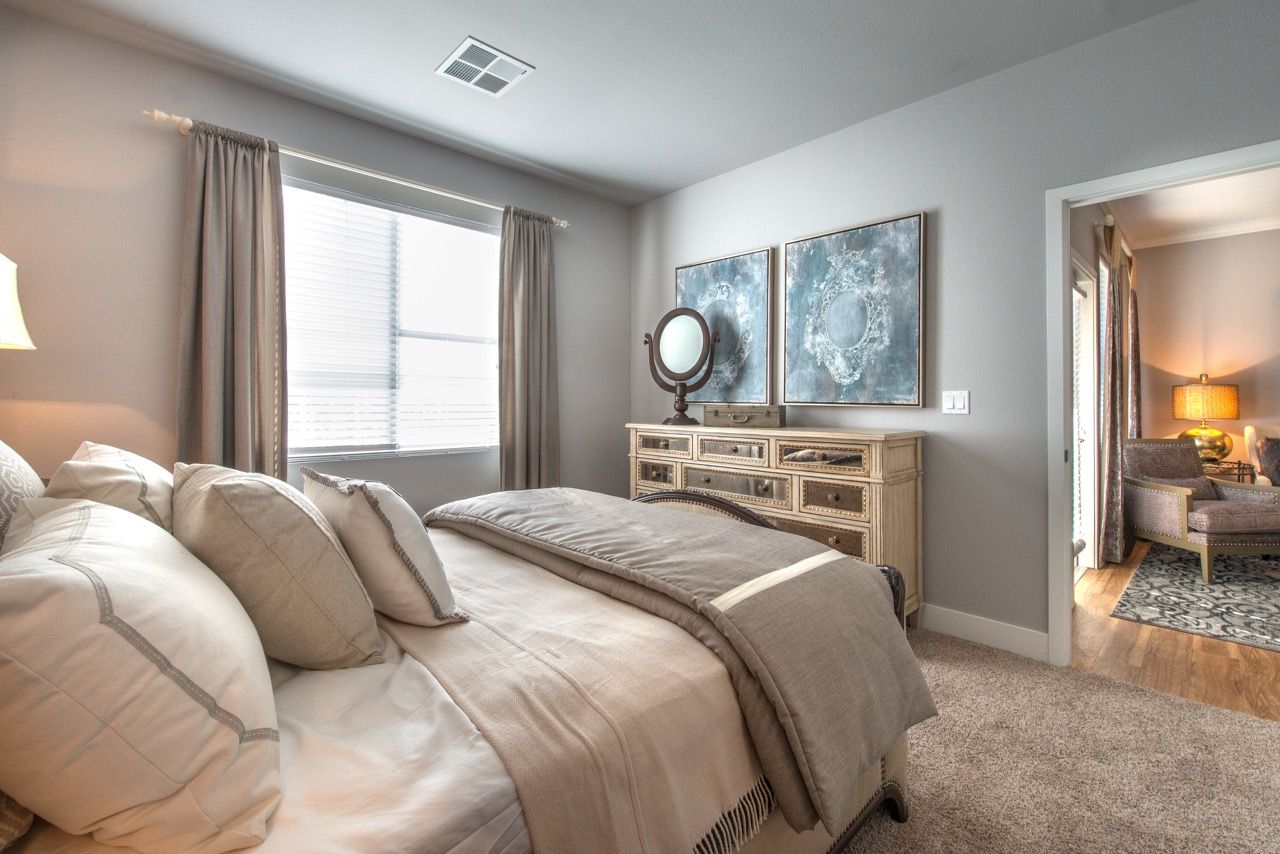 Bedroom in a modern apartment with a bed, dresser, and window.