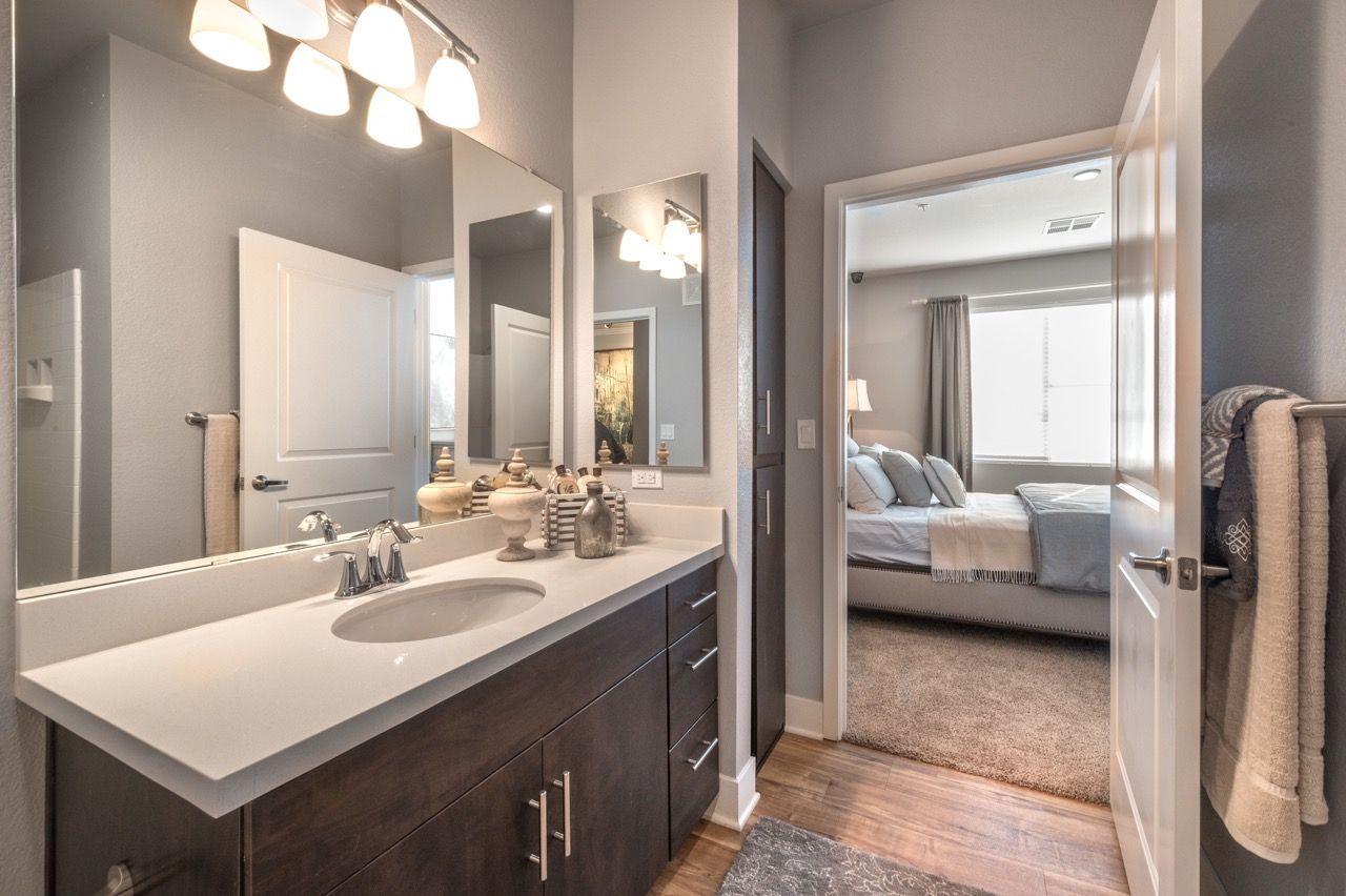 Bathroom vanity with double sink, mirrors, and doorway to a bedroom.