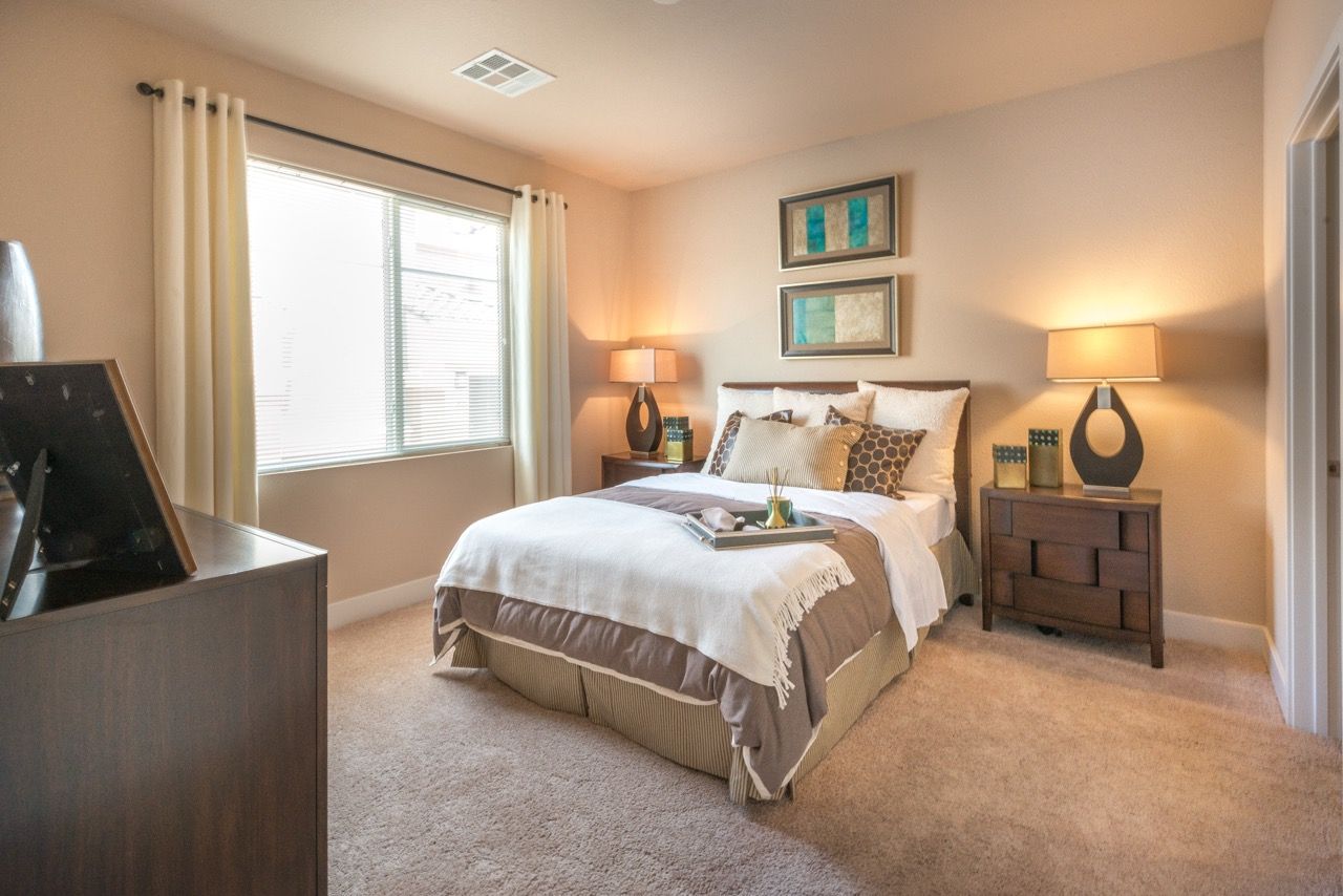 Furnished bedroom with a queen bed, two nightstands, lamps, and a large window.