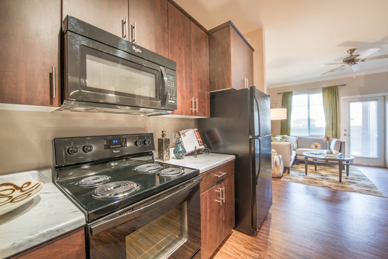 Kitchen in an apartment with dark wood cabinets, black stove, microwave, and refrigerator.