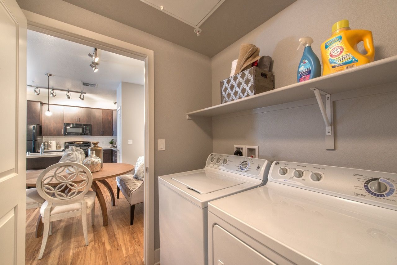 In-unit laundry area with a washer and dryer, plus a storage shelf; view into dining/kitchen.