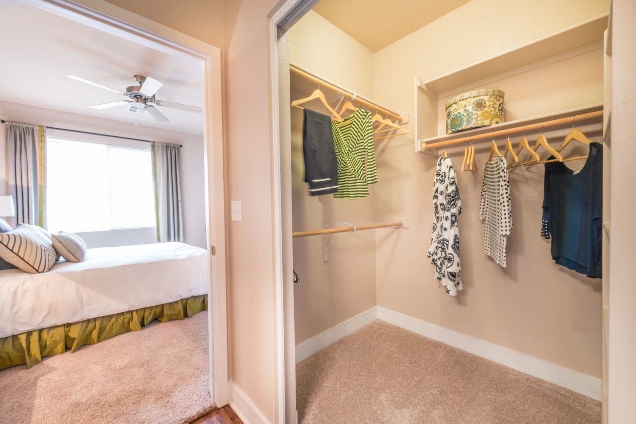 Bedroom with an open walk-in closet showing clothes on hangers beside the bed.