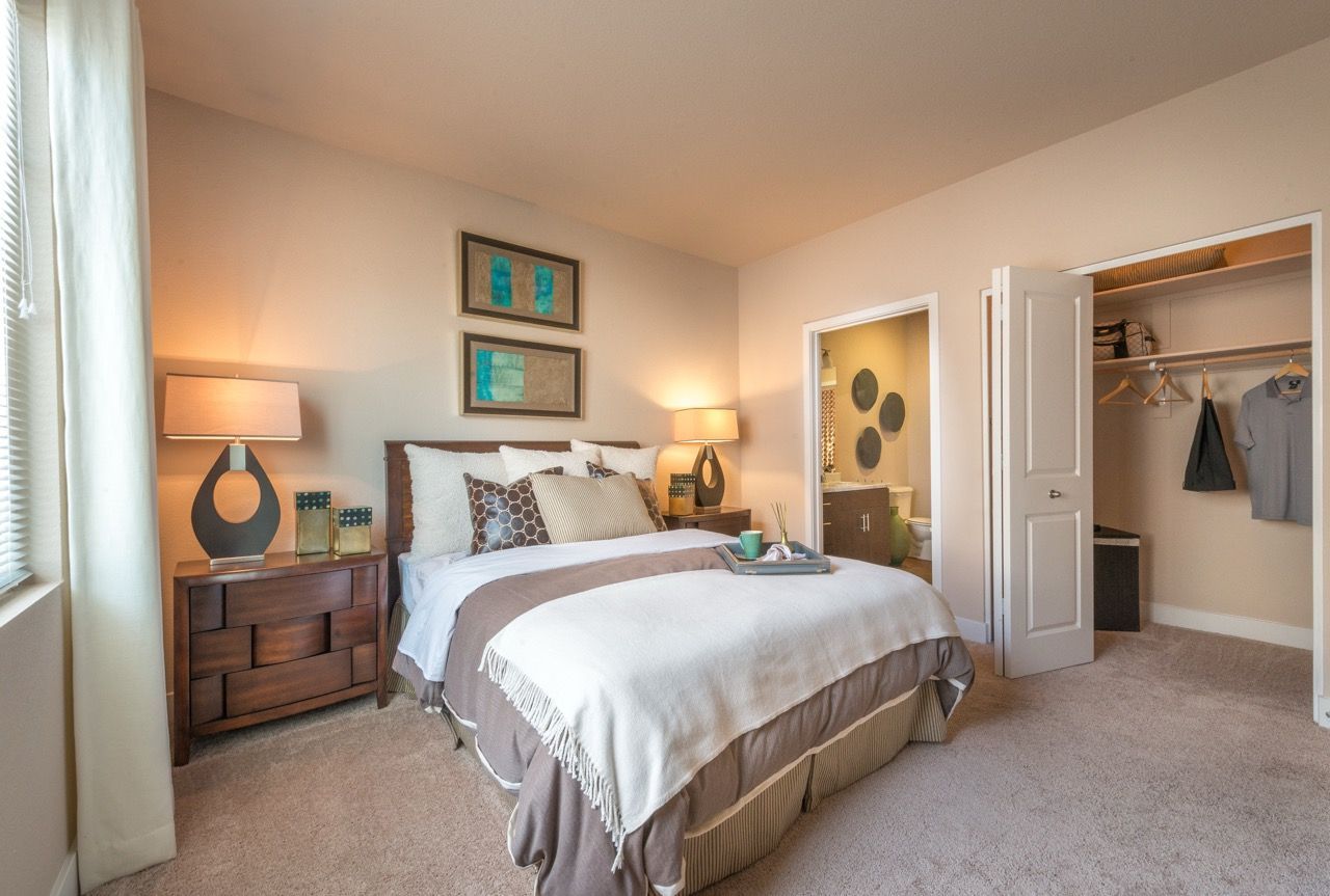Bedroom in an apartment with a large bed, two matching nightstands, lamps, and an open closet.