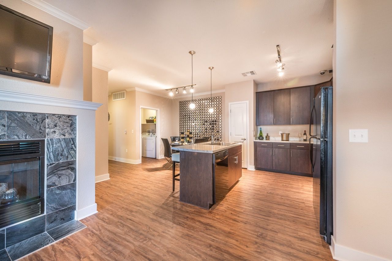 Open-concept kitchen with island, dark cabinetry, stainless appliances, and a living area with a fireplace.