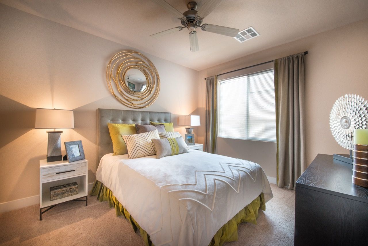 Bedroom in an apartment with a tufted headboard bed, nightstands, lamps, and a window.