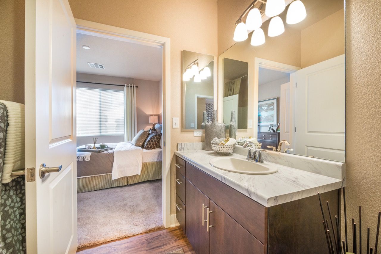 Bathroom vanity with marble countertop and mirror; doorway to a bedroom.