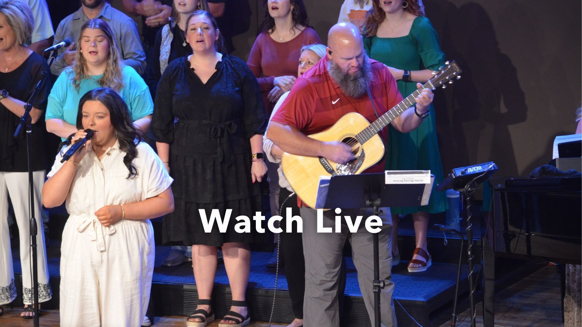 A man is playing a guitar in front of a choir.