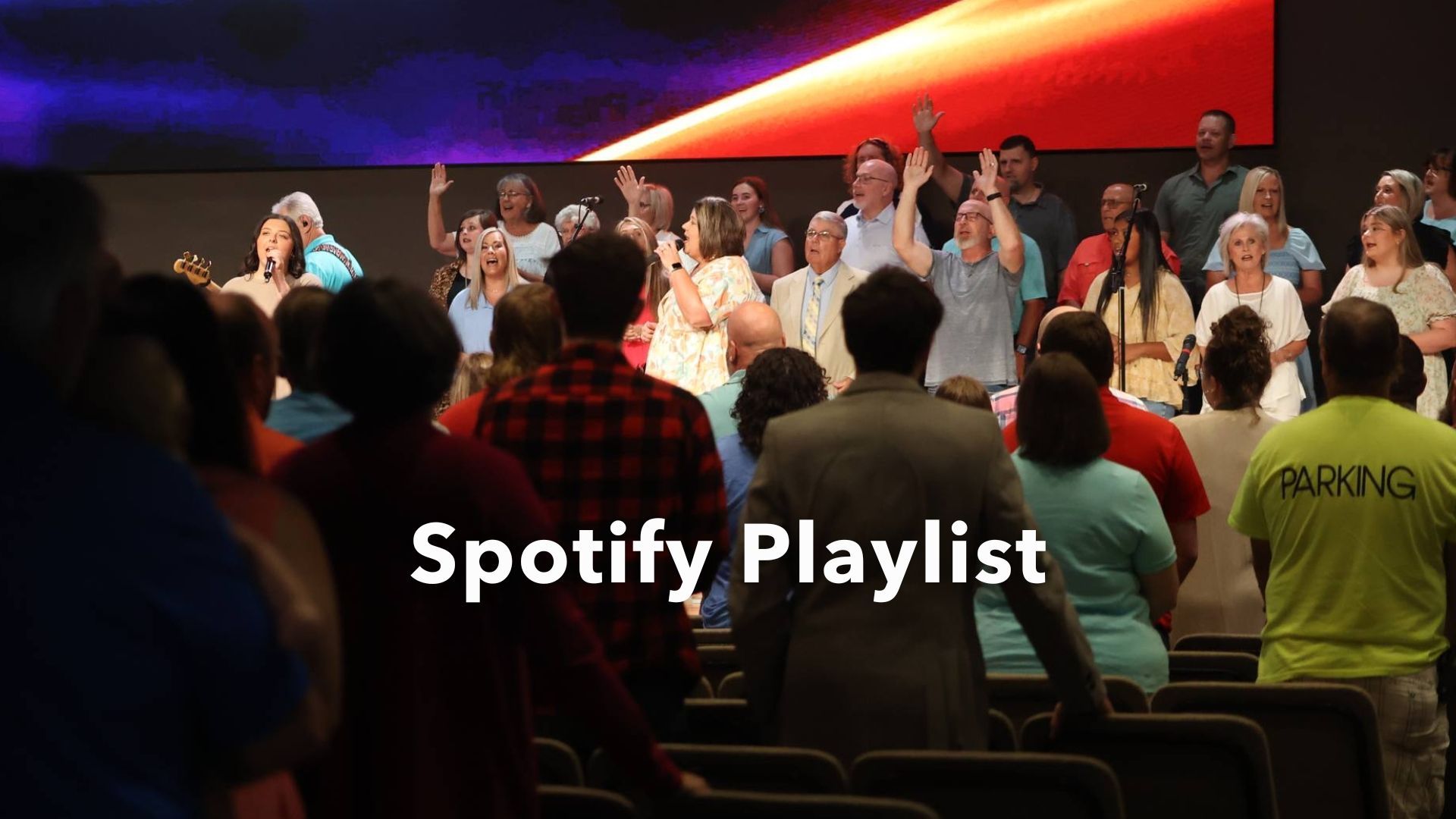 A large group of people are singing in a church with the words spotify playlist above them