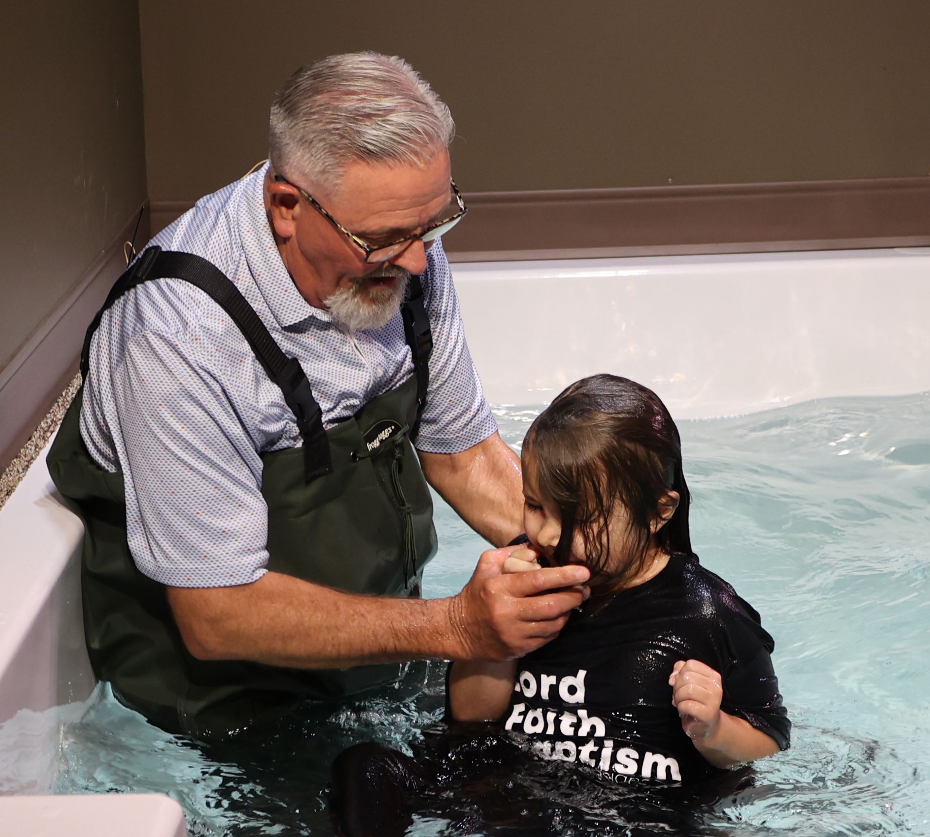 A man is helping a little girl get baptized in a bathtub.