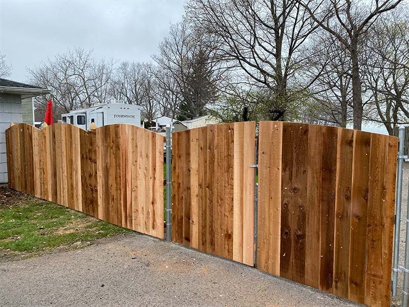 A wooden fence with a metal gate in front of a house.