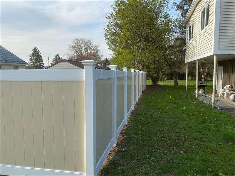 A white and tan fence is in the backyard of a house.