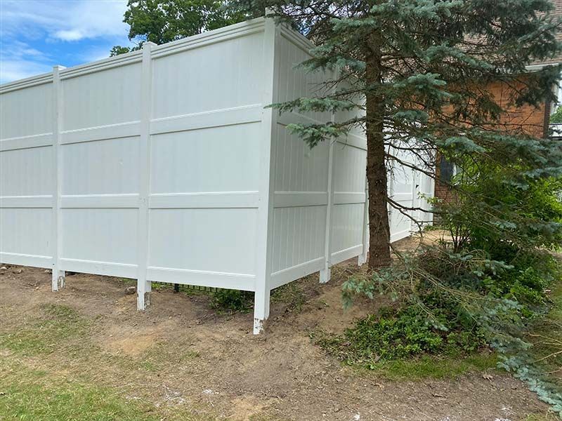 A white fence is sitting on top of a dirt hill next to a tree.