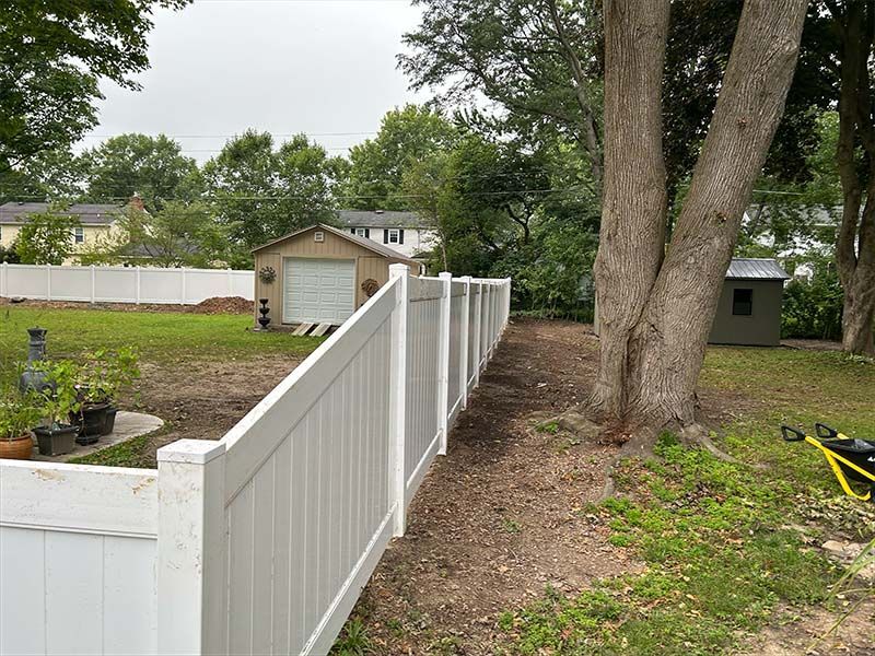 A white fence surrounds a yard with trees and a garage in the background.