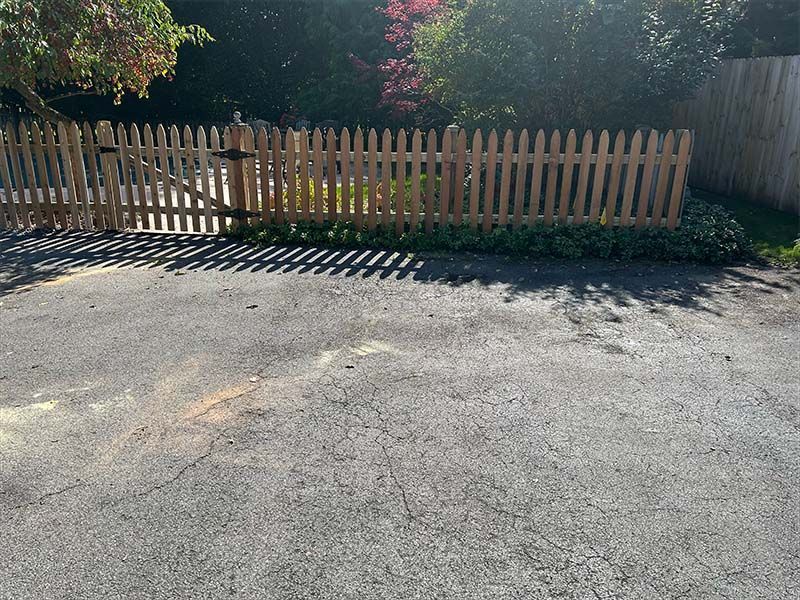 A wooden picket fence is in the middle of a parking lot.