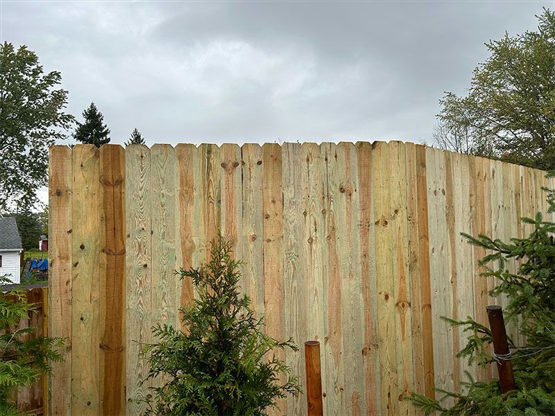 A wooden fence with trees and a house in the background