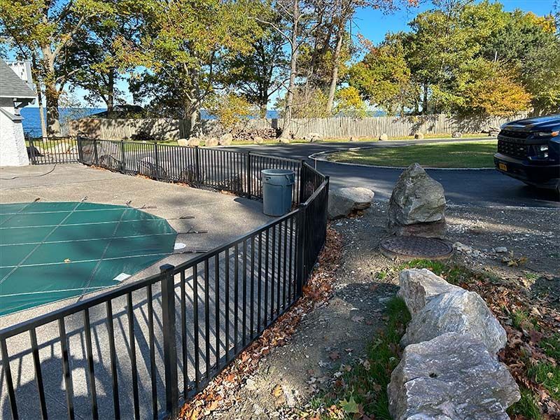 A black fence surrounds a swimming pool with a green cover.