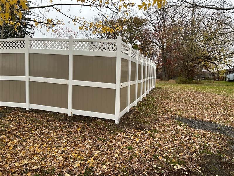 A white and brown fence is surrounded by leaves in a yard.