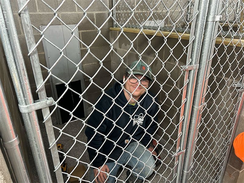 A man is sitting behind a chain link fence.