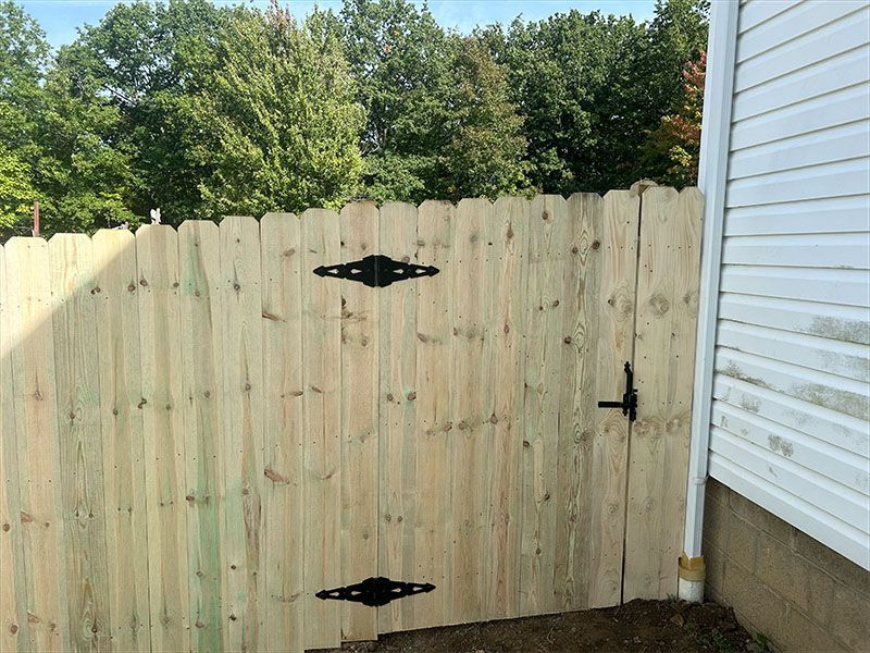 A wooden fence with a black gate is next to a white house.