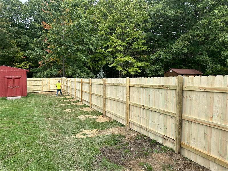 A man is standing next to a wooden fence in a backyard.