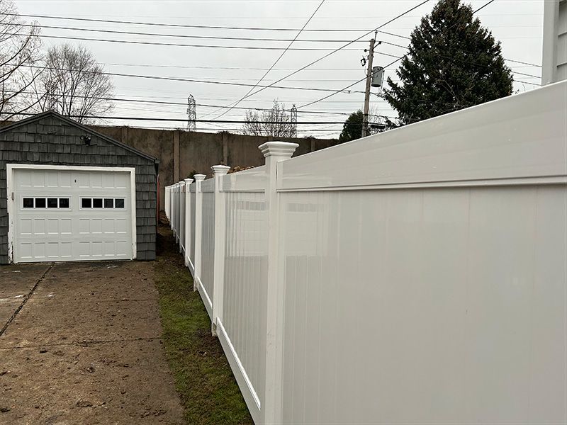 A white fence surrounds a garage with a white garage door.