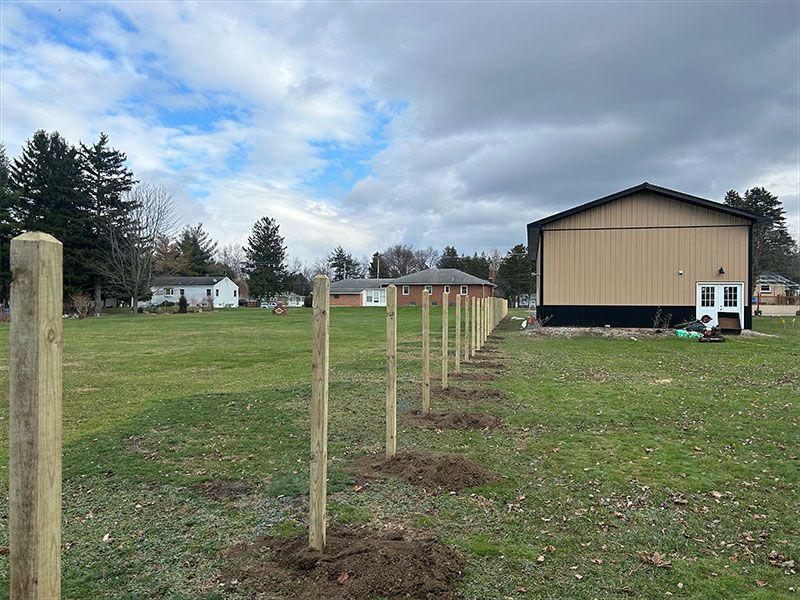 A fence is being built in a field with a barn in the background.