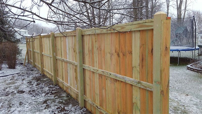 A wooden fence is sitting in the snow next to a trampoline.