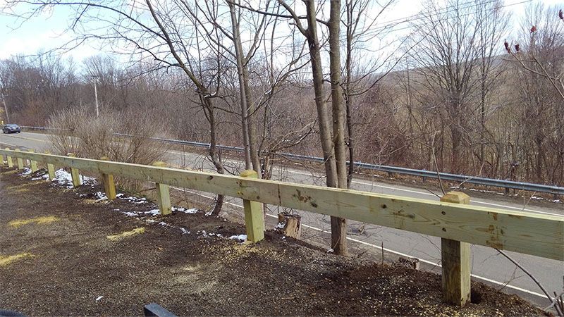 A wooden fence along the side of a road with trees in the background.