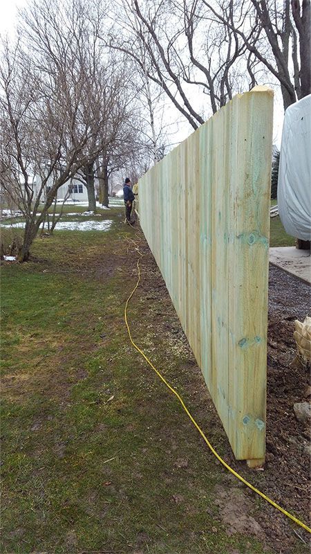 A man is standing next to a wooden fence in a yard.