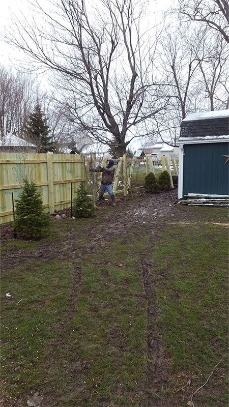 A man is working on a wooden fence in a backyard.
