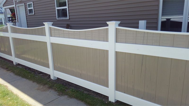 A brown and white fence is in front of a brown house.