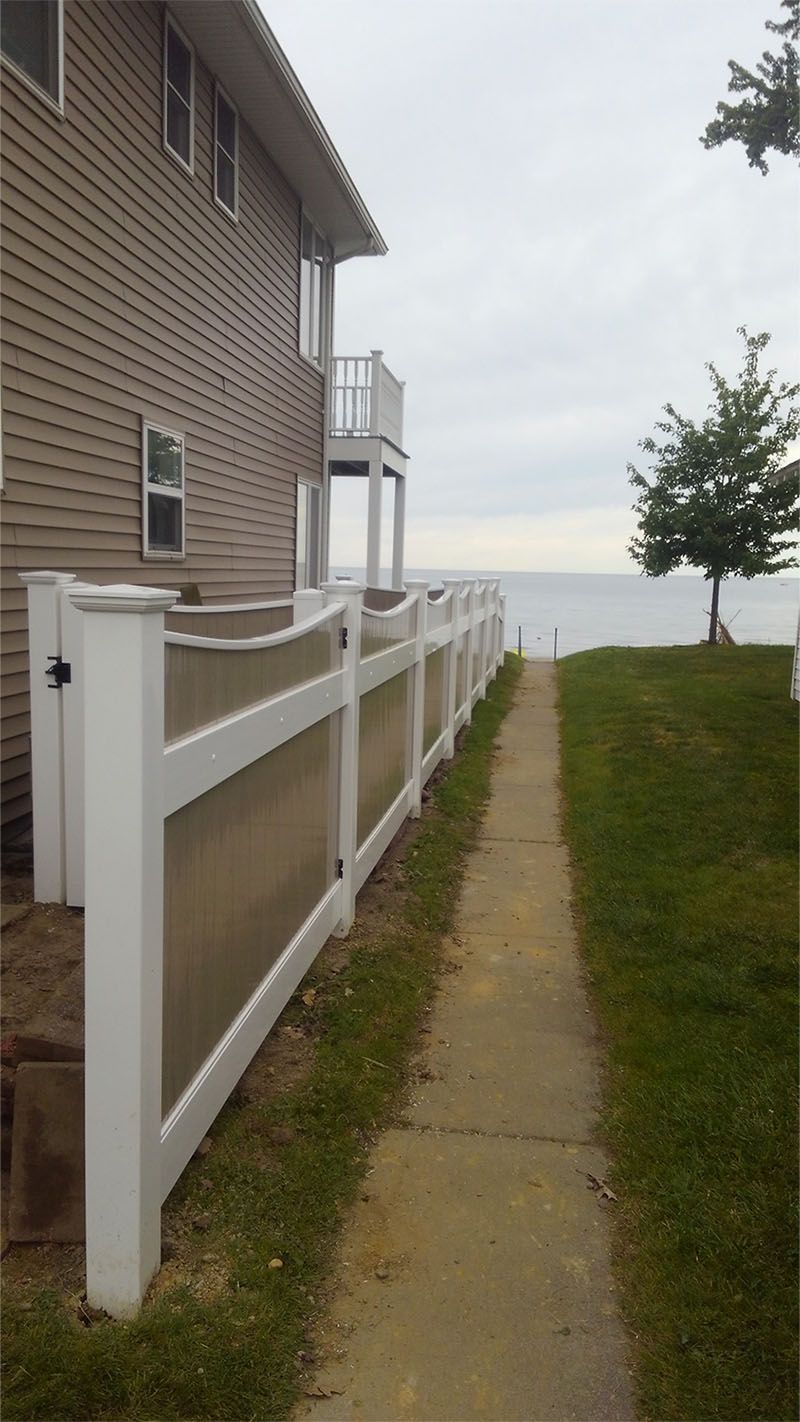 A white fence along a sidewalk leading to a house with a view of the ocean.