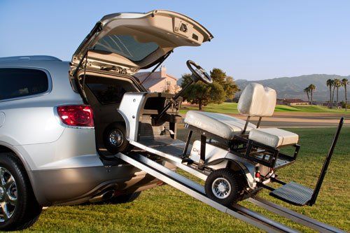 A golf cart is being towed by a car with the trunk open.