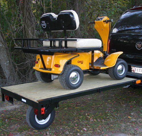 A yellow golf cart is on a trailer attached to a black suv