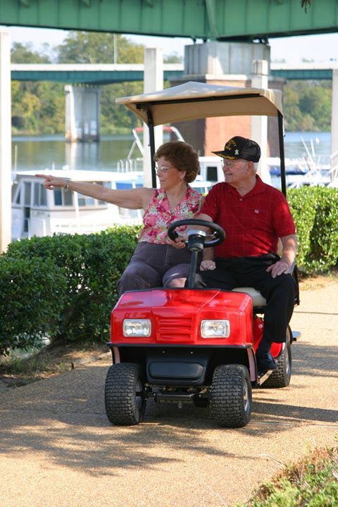 A man and a woman are riding a red golf cart.