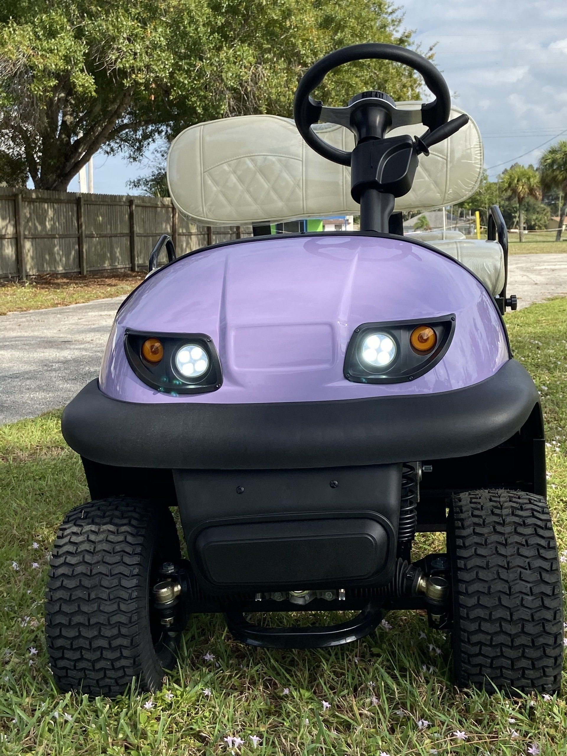A purple golf cart is parked in the grass.