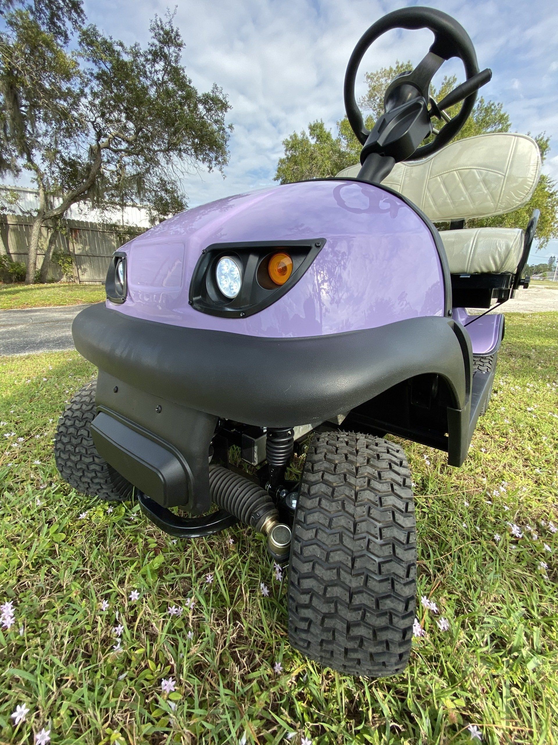 A purple golf cart is parked in the grass.