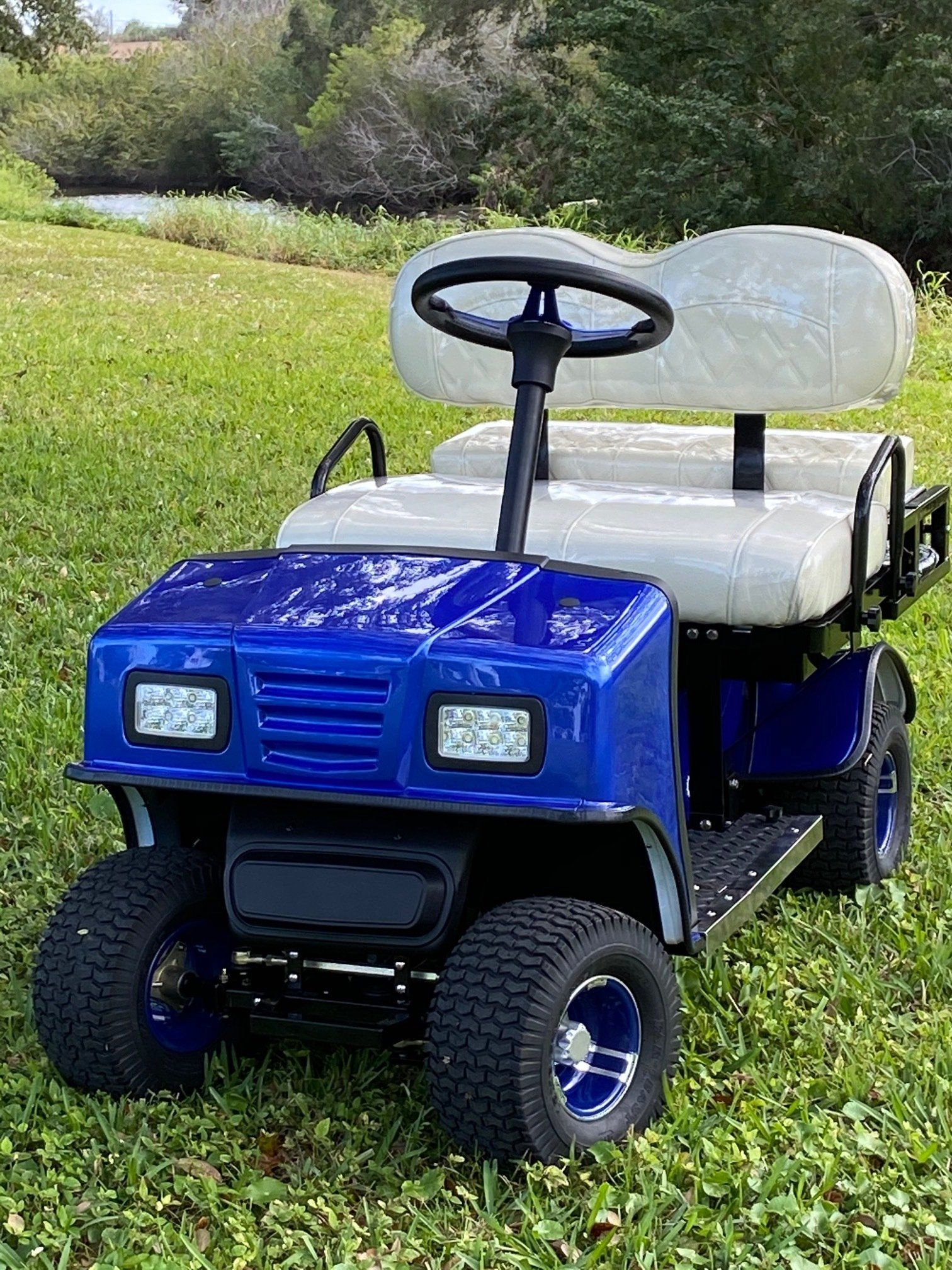 A blue golf cart with white seats is parked in the grass.