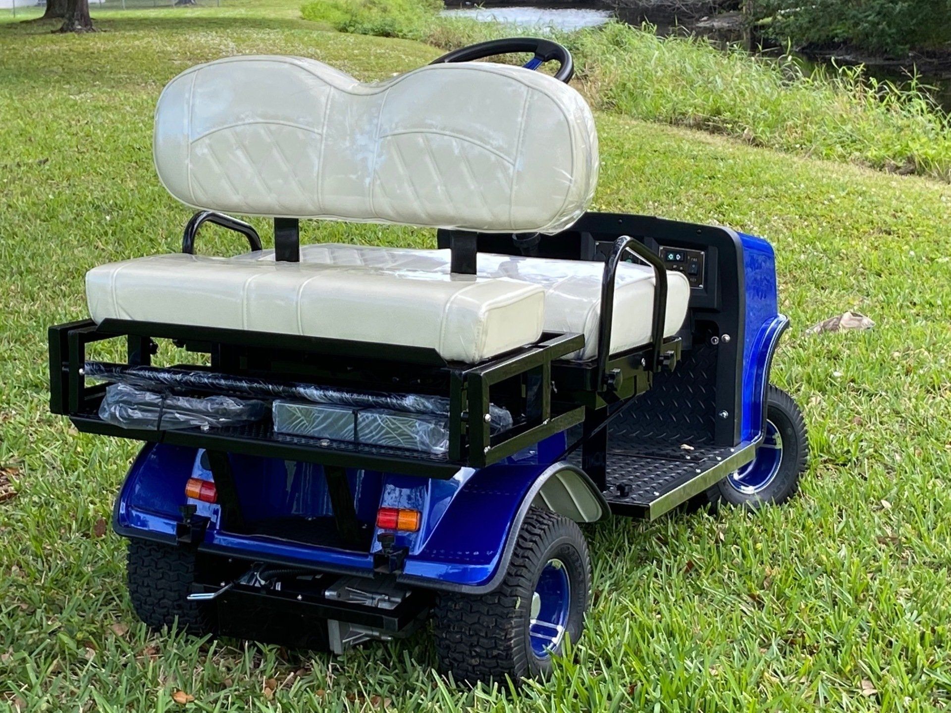 A blue golf cart with white seats is parked in the grass.