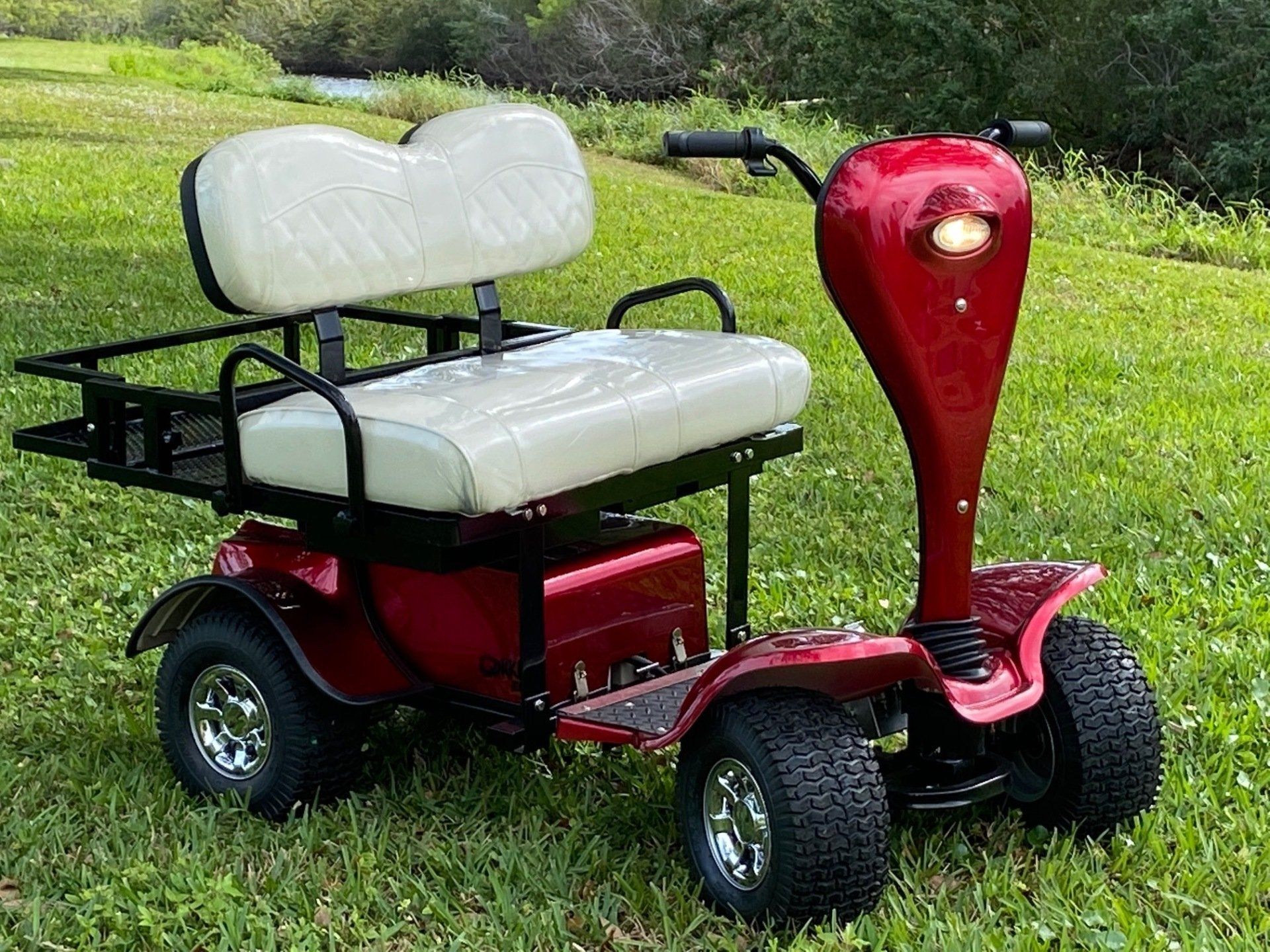 A red golf cart with a white seat is parked in the grass.