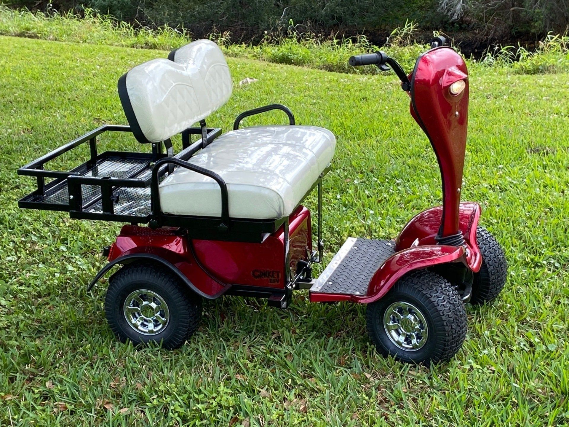 A red Cricket with a white seat is parked in the grass.